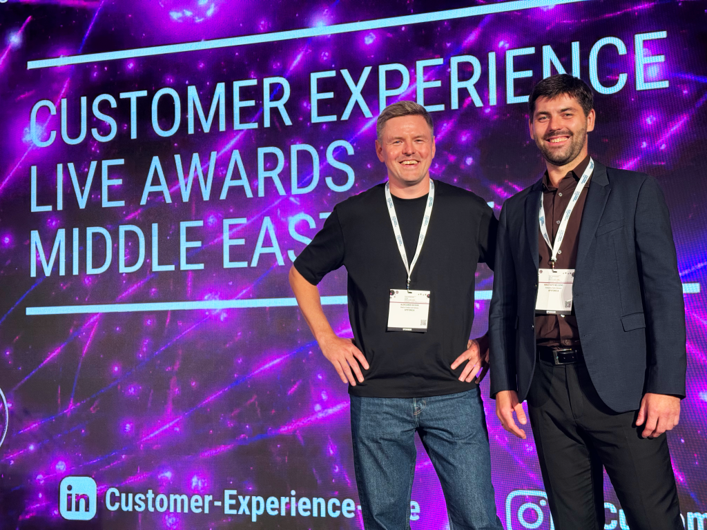 Apifonica representatives Alexander Mishin and Kristaps Nelsons pose in front of the Customer Experience Live Awards Middle East event backdrop.